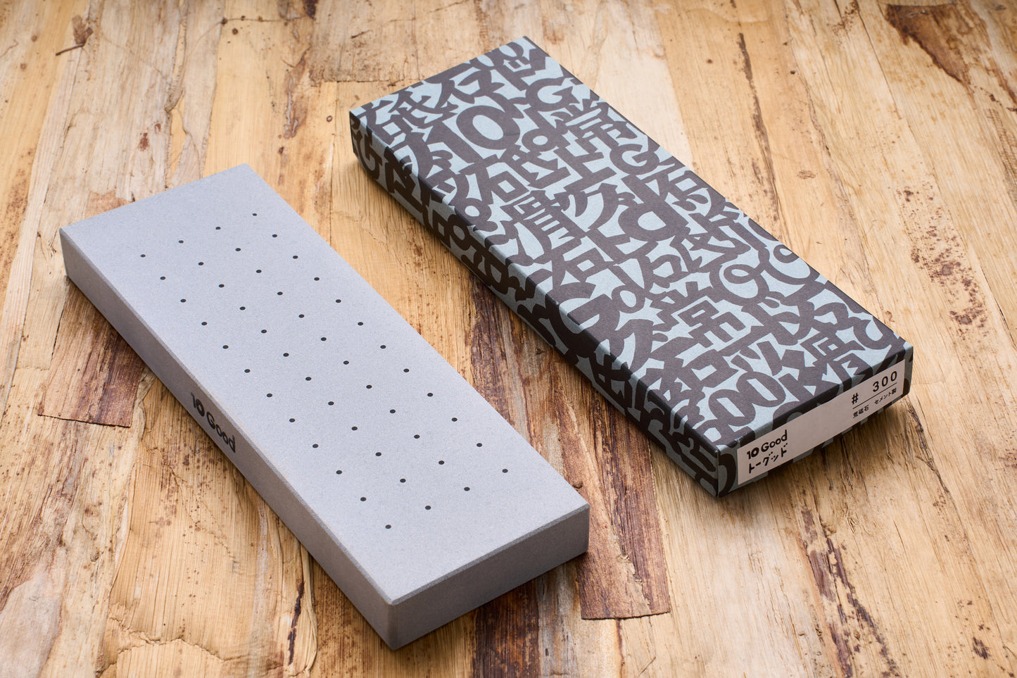 10 Good Coarse 300 Grit Stone with dotted surface, shown with its decorative sleeve, ideal for sharpening beginners, on a wooden tabletop.