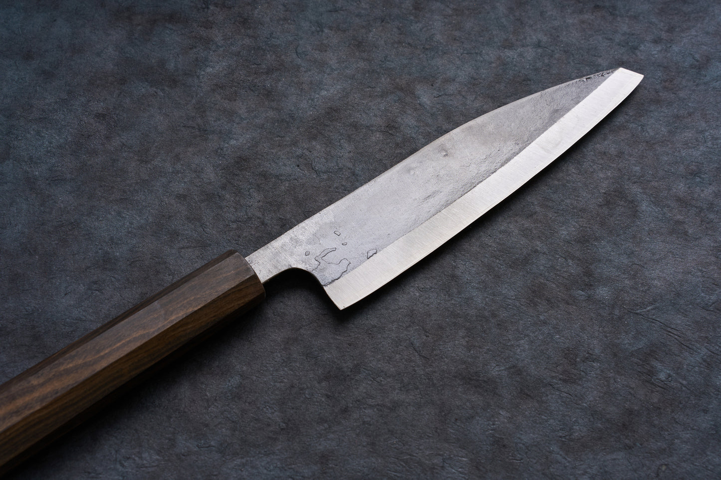 Fukamizu Ginsan Satuma no Kami Ko-Bunka 150mm knife, featuring a steel blade and dark wooden handle, displayed diagonally on a slate-like surface.