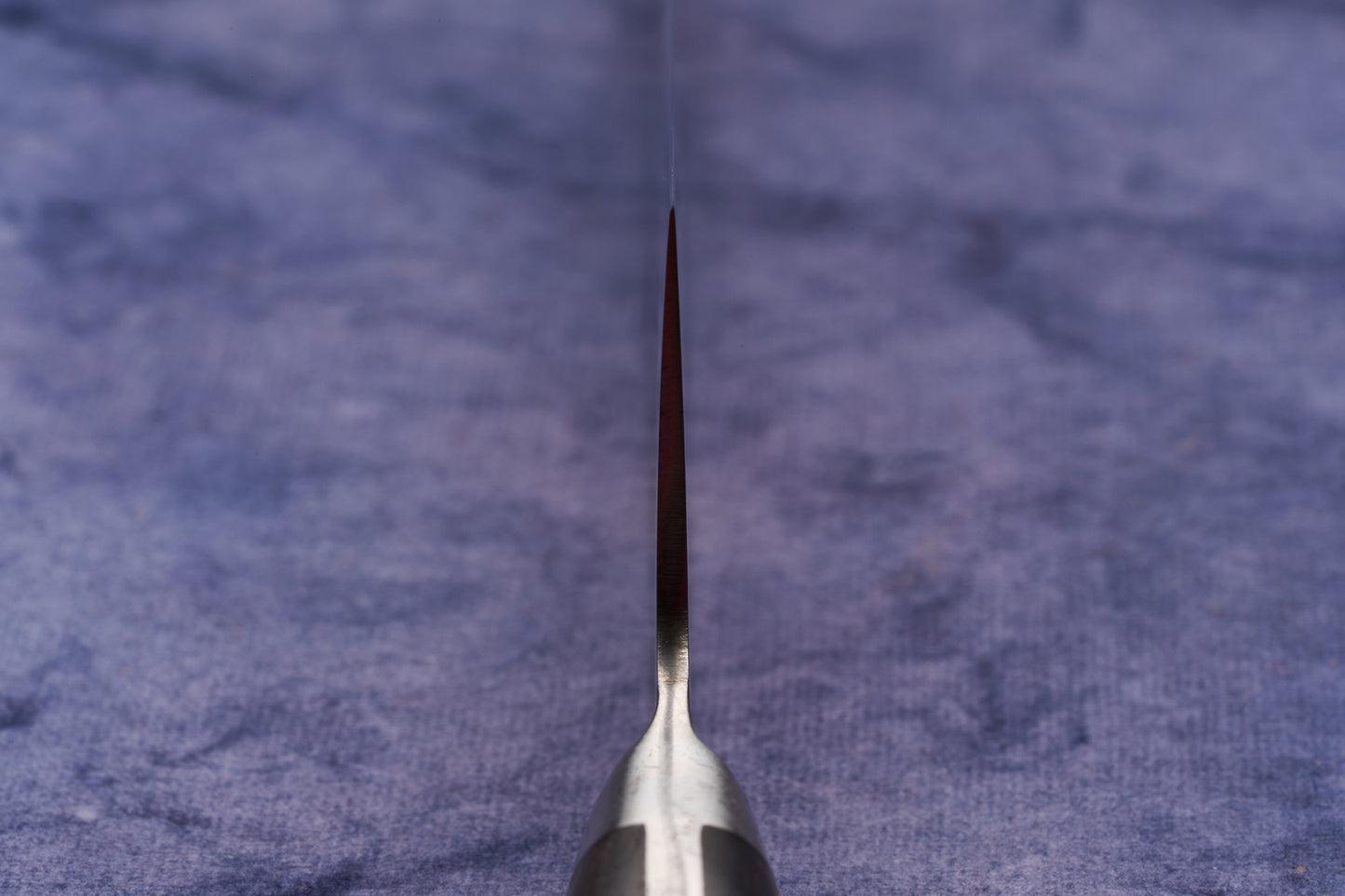 Hazaki Classic Black Utility 135mm knife, standing edge-up on a blue cloth, showcases its thin, sharp blade expertly forged in Japan. The handle, crafted from Canadian wood, complements its sleek design.