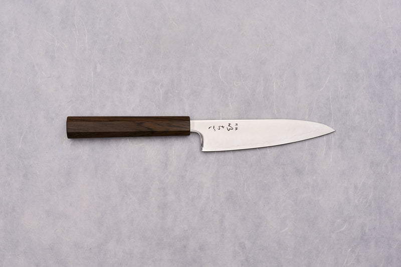 ICHIGO SLD Migaki Petty 130mm Japanese kitchen knife features a polished stainless-steel blade with a hamon line and kanji, paired with a dark octagonal wooden handle, ideal for precise kitchen tasks.