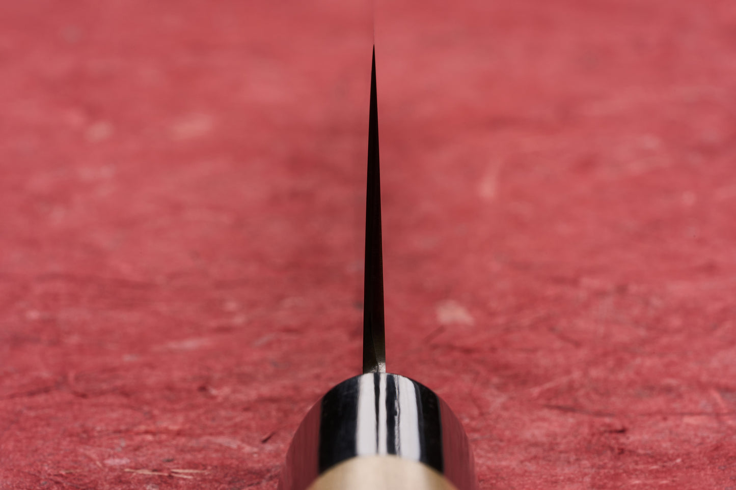 Masamoto KS Hongasumi Kiritsuke Gyuto 240mm knife, thin blade rising from dark bolster and wooden handle, showcased on a red surface, epitomizing precision and craftsmanship from legendary Tokyo-based knifemaker.