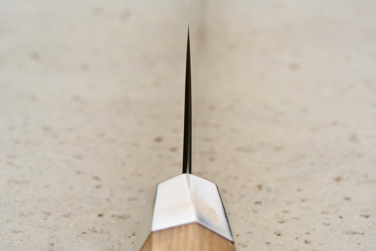 Mcusta Zanmai Beyond Kiritsuke Sujihiki 270mm knife, showcasing a thin blade with a metal bolster and a Hinoki wood handle, resting on a speckled stone-like surface, embodying luxury and precision craftsmanship.