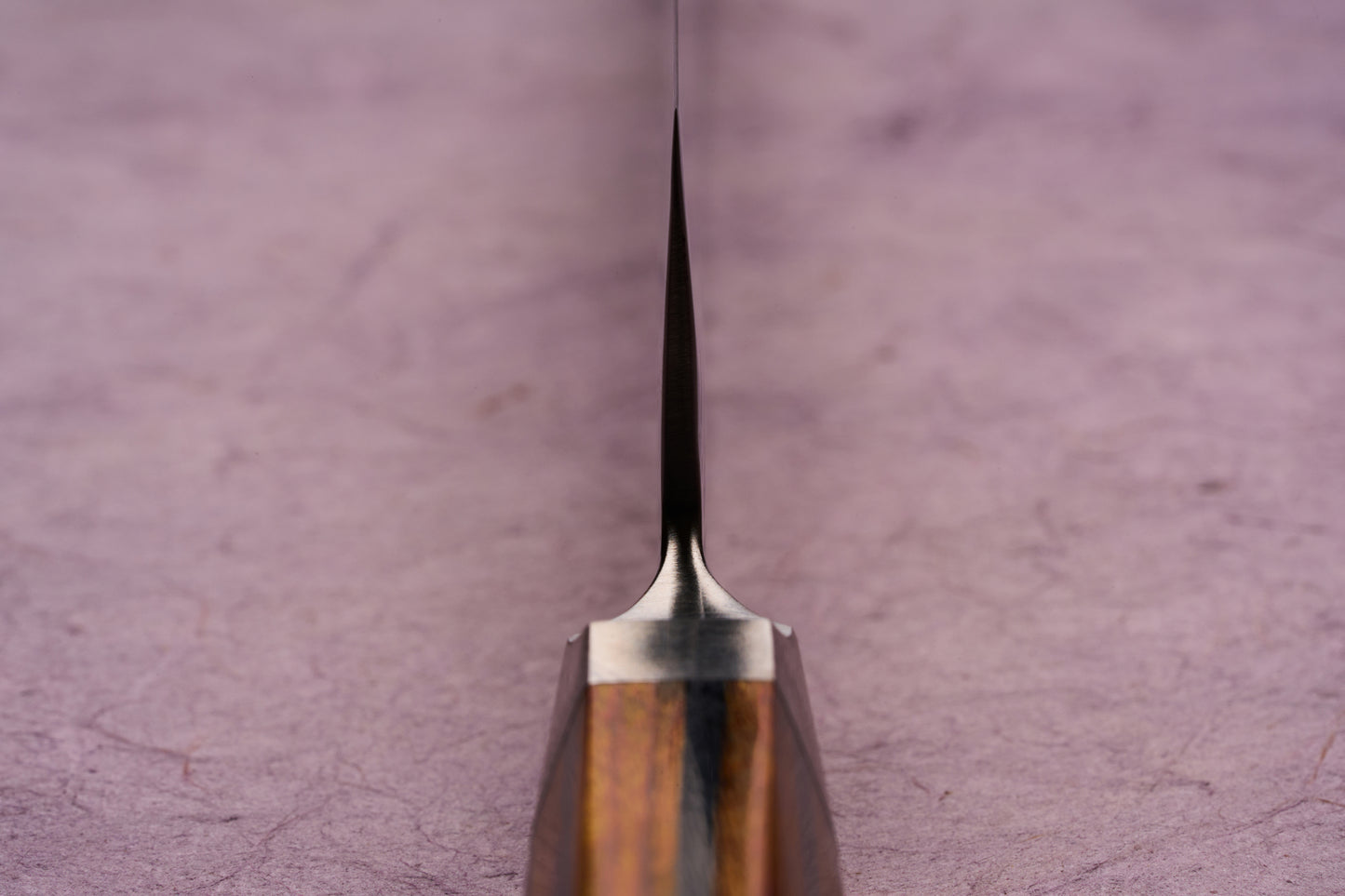 Ono Knife Suzukaze SG2 Tsuchime Damascus Petty 150mm, viewed from the handle, showcases its thin, tapering blade. The wooden handle and metal bolster subtly visible, highlight craftsmanship and precision.