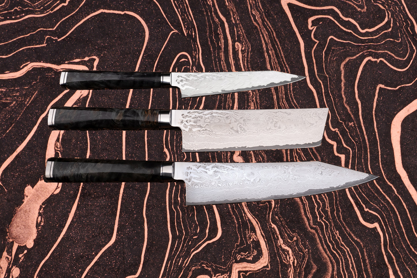Ryusen Oukokuryu Knife Set featuring three Damascus-style blades with dark handles, displayed on a marbled surface, showcasing exceptional Japanese craftsmanship and design.