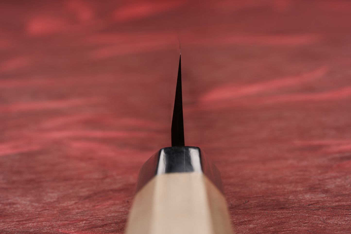 Close-up of the Touroku Sakai Shirogami Kasumi Yanagiba 240mm knife, showcasing its sleek blade edge and elegant handle on a textured red surface, reflecting exceptional Japanese craftsmanship.