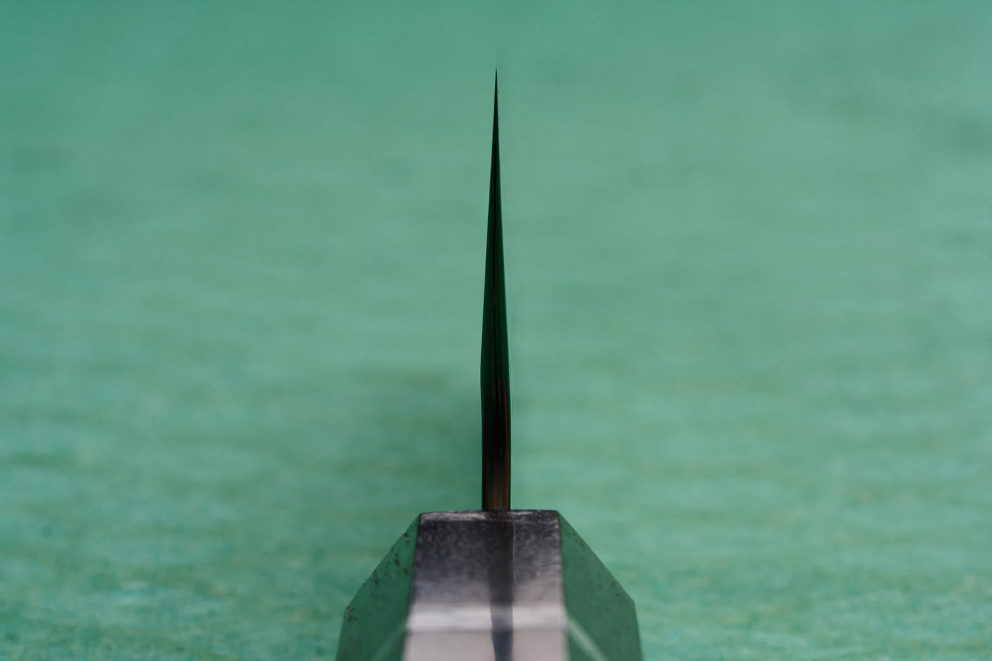 Yoshimi Kato SG2 Hyo Santoku 165mm knife, viewed edge-on, showcasing its razor-sharp blade against a green background, epitomizing the excellence of Japanese craftsmanship from Knifewear.