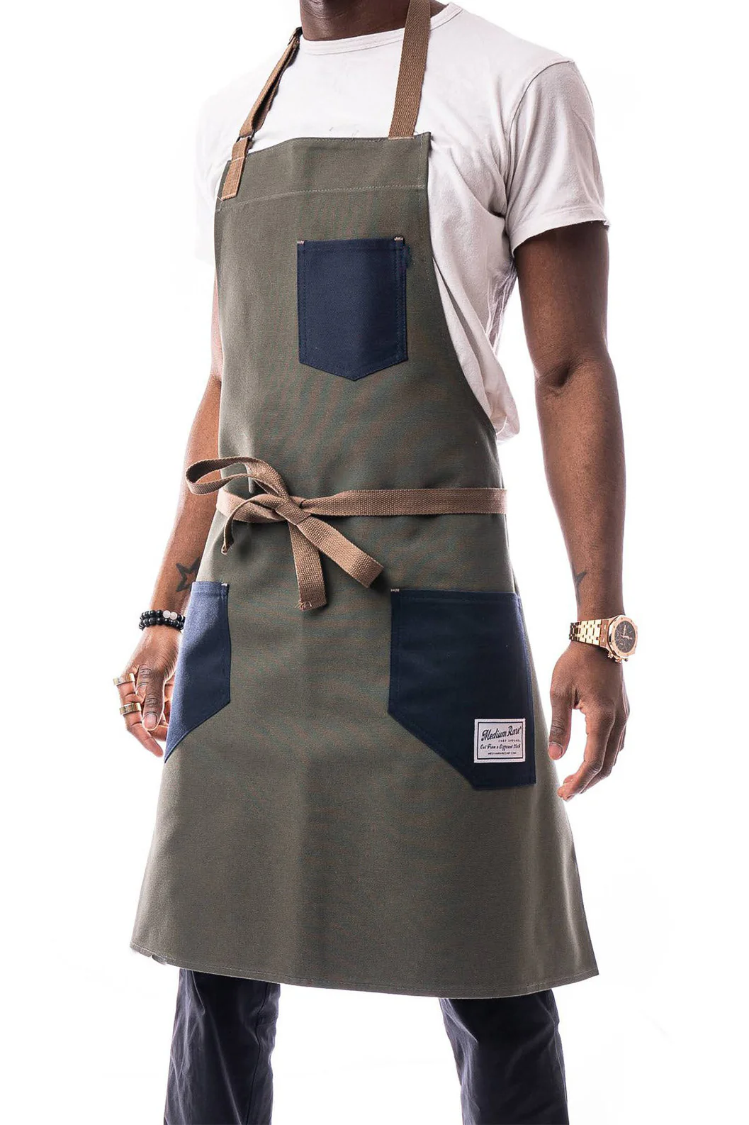 Person wearing Medium Rare Kayle Apron in olive green with navy pockets and brown straps, showcasing durable design for culinary professionals and home chefs.
