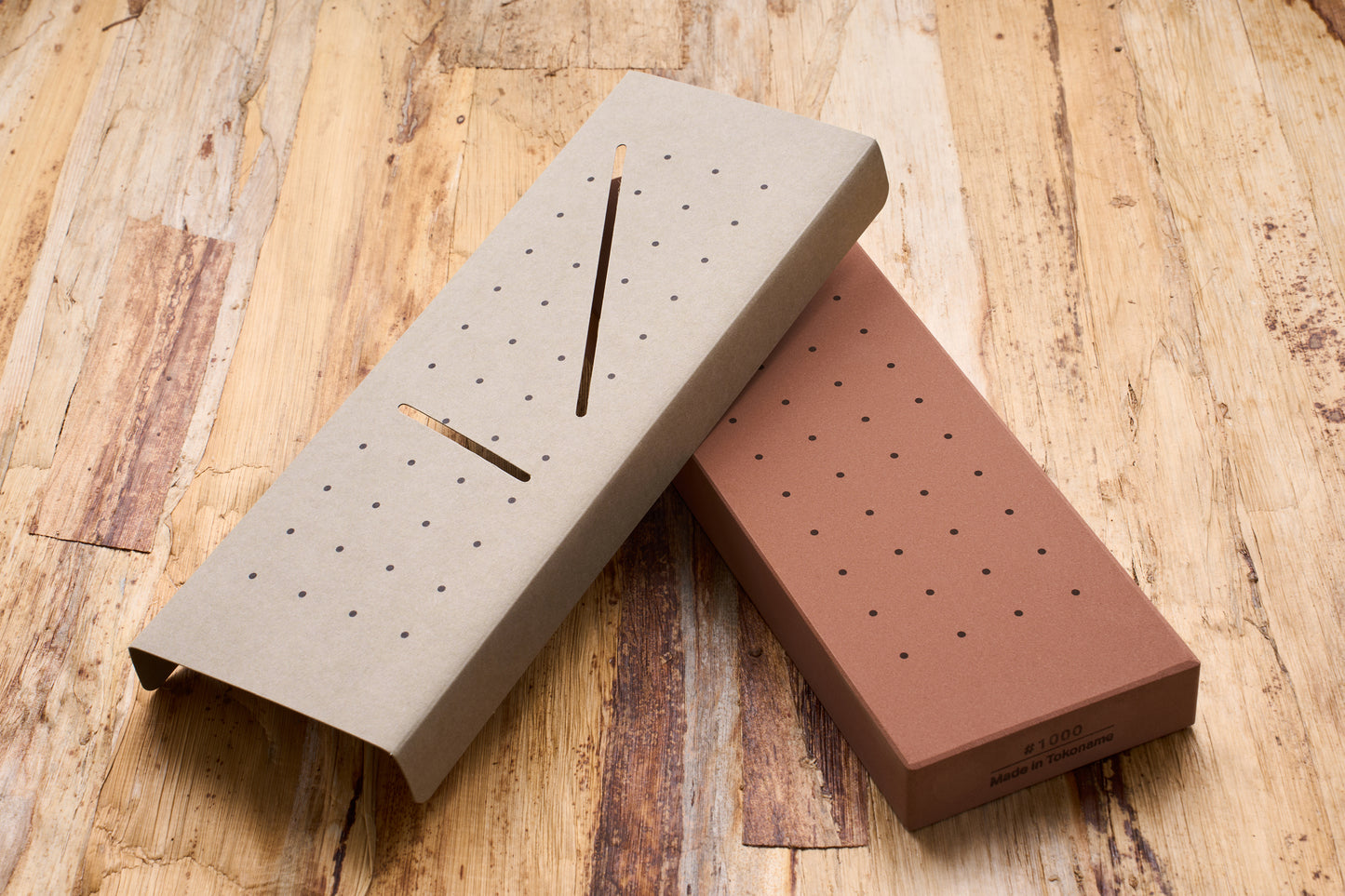 10 Good Medium 1000 Grit Stone with dotted surface and cardboard sleeve, ideal for sharpening beginners, displayed on a wooden tabletop.