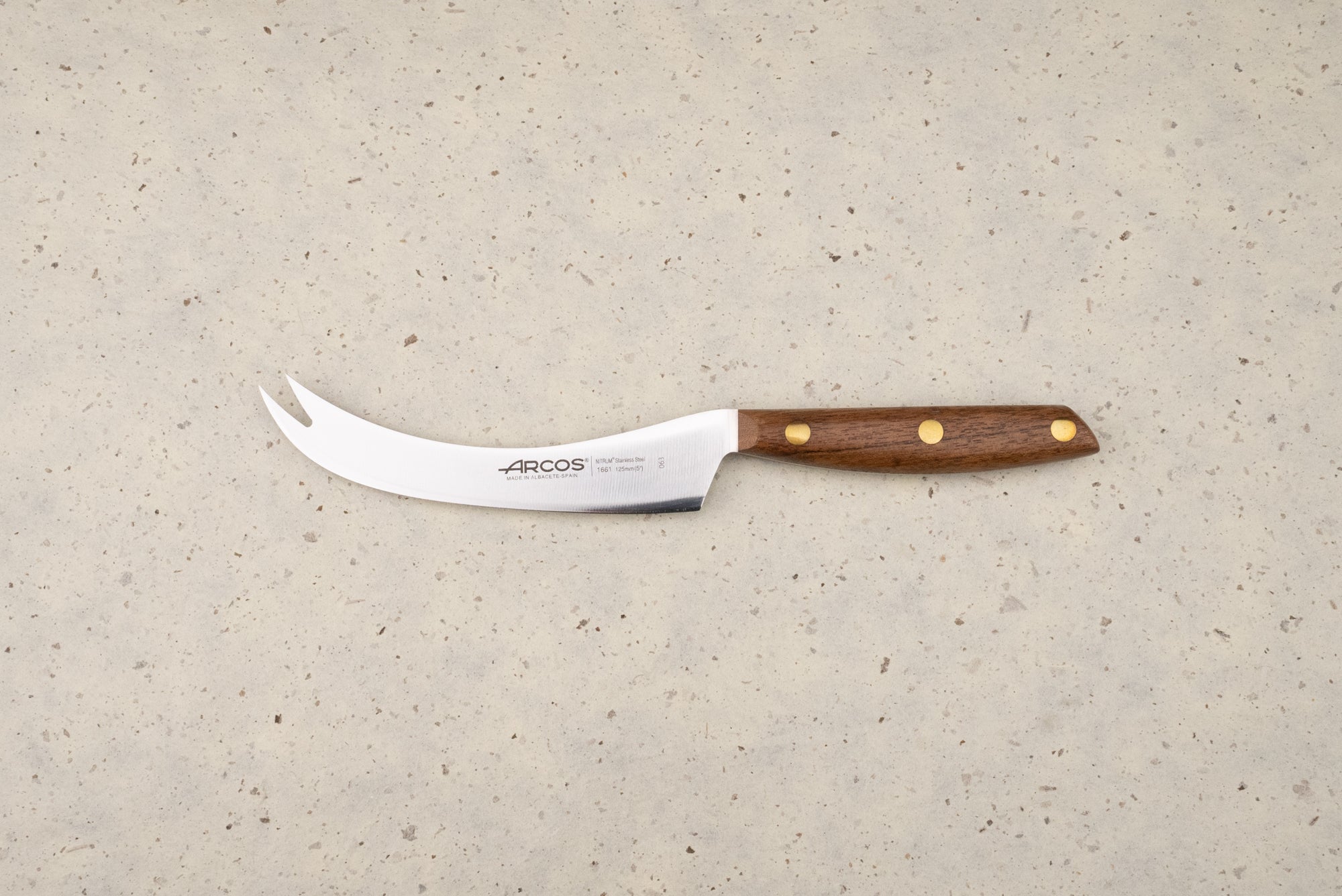 Arcos Nordika 125mm Manchego Knife features a curved blade with a two-pronged tip, perfect for slicing cheese. Its wooden handle and three-rivet construction showcase craftsmanship from Albacete, Spain.