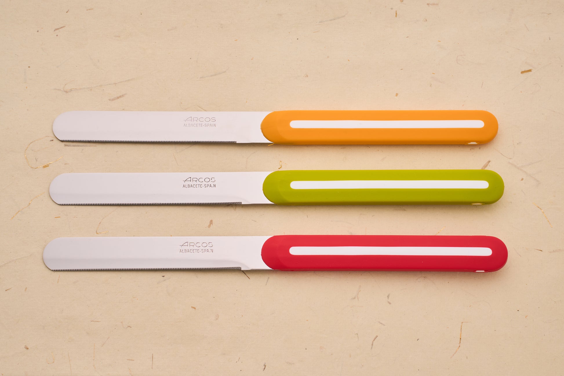 Arcos Linea 3pc Table Knife Set with serrated stainless steel blades and vibrant plastic handles, showcasing Spanish craftsmanship.