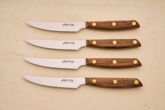 Arcos Nordika 4pc Steak Knife Set with stainless-steel blades and dark wood handles, crafted in Spain, showcasing precision and quality from a historic knife-making legacy.