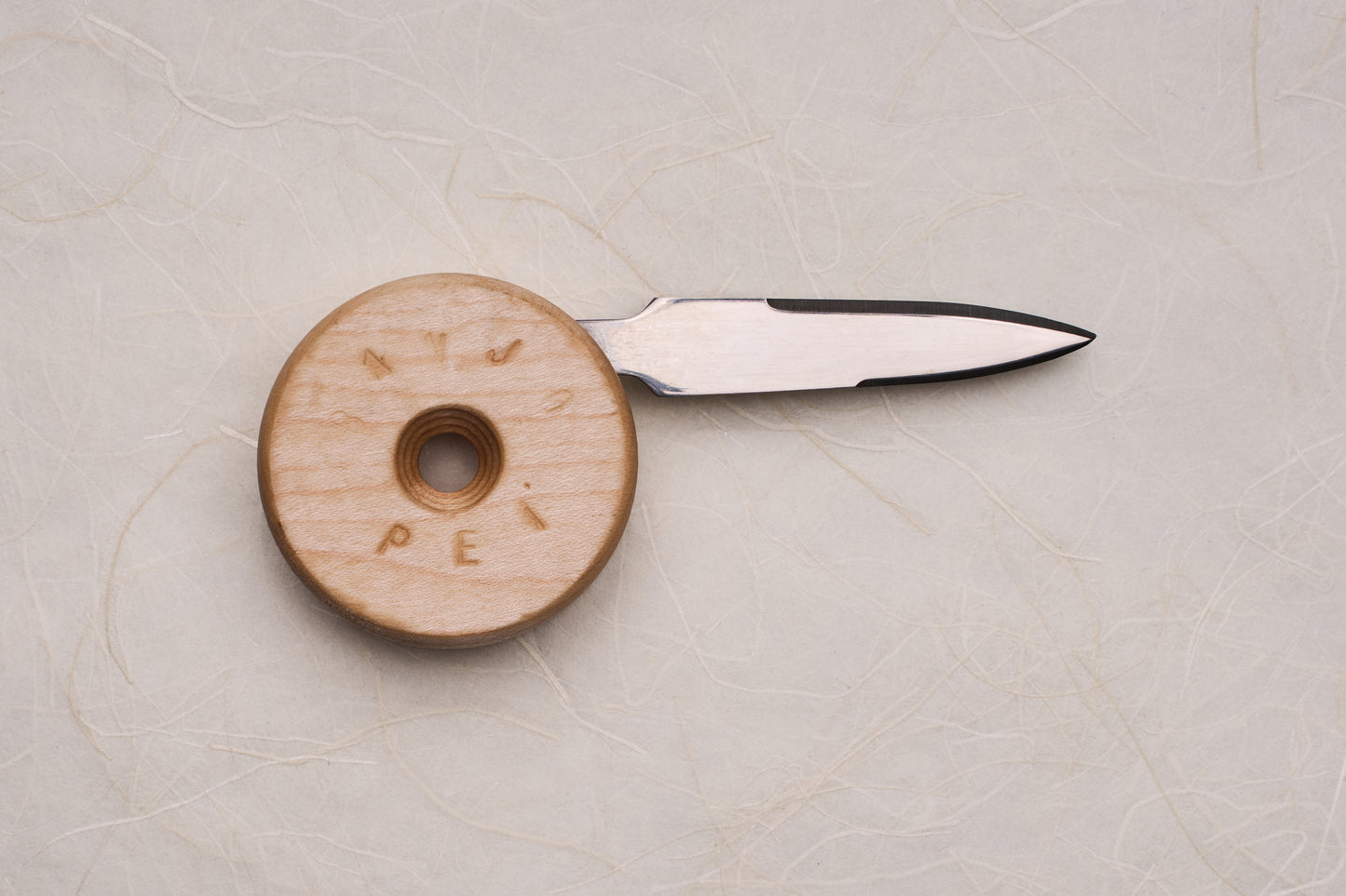 Banjo Oyster Knife with a double-edged blade tucks into a circular wooden handle, designed for ergonomic shucking. Inspired by skateboard wheels, crafted in Canada, perfect for oyster enthusiasts.