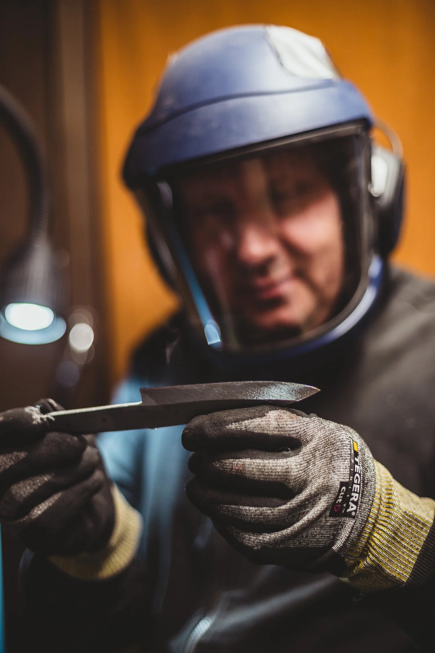 A person in a workshop sharpens the Resqknives Korpi Camp Kitchen Knife, showcasing its Flamed Finnish Birch handle and recycled stainless steel blade.