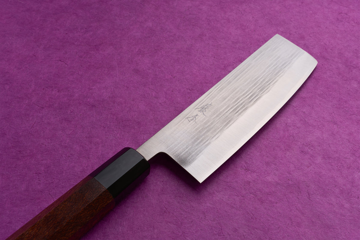Fujimoto AS Sazanami Nakiri 165mm on a textured surface, featuring a stainless-steel, Damascus-patterned blade with kanji engravings and an octagonal wooden handle with black ferrule.