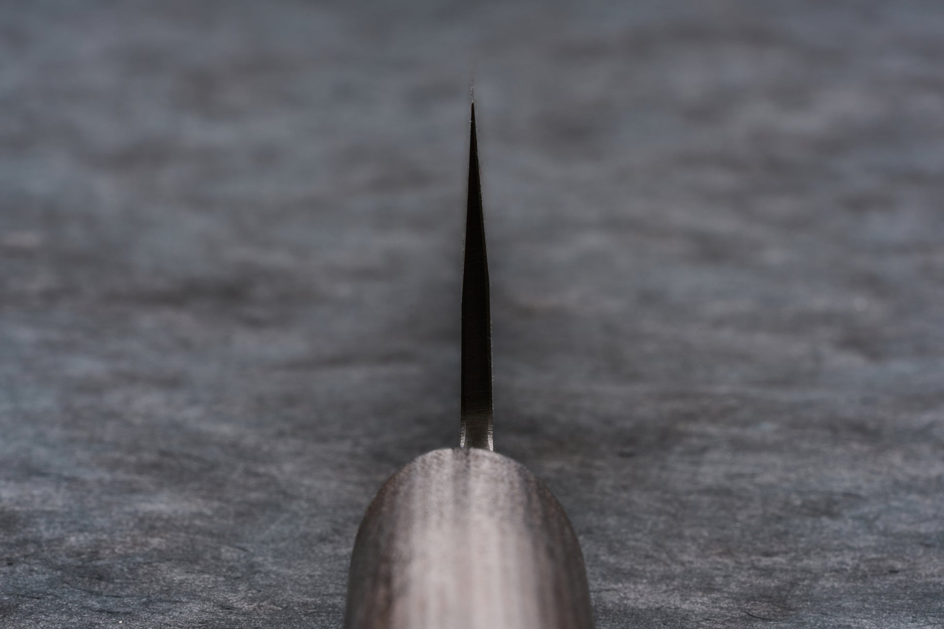 Fujimoto Nashiji Honesuki 150mm knife, with its distinctive wa handle in the foreground, rests on a stone surface. The thin blade extends away, showcasing expert craftsmanship and a unique nashiji finish.