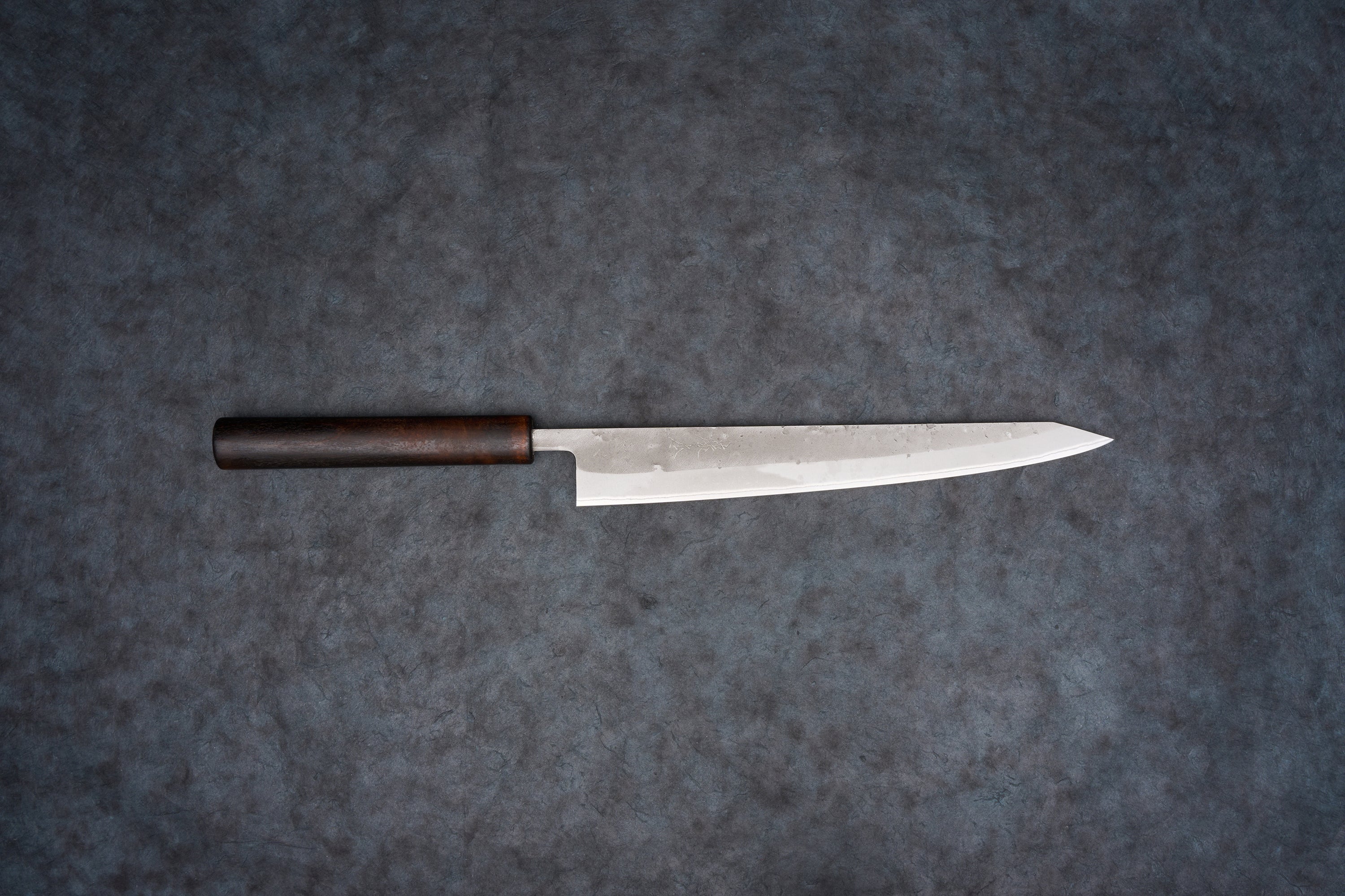 Fujimoto Nashiji Sujihiki 240mm: A sleek Japanese slicing knife with a slender steel blade and dark wooden handle, ideal for precise cuts like sashimi, featuring a carbon steel core with stainless steel protection.