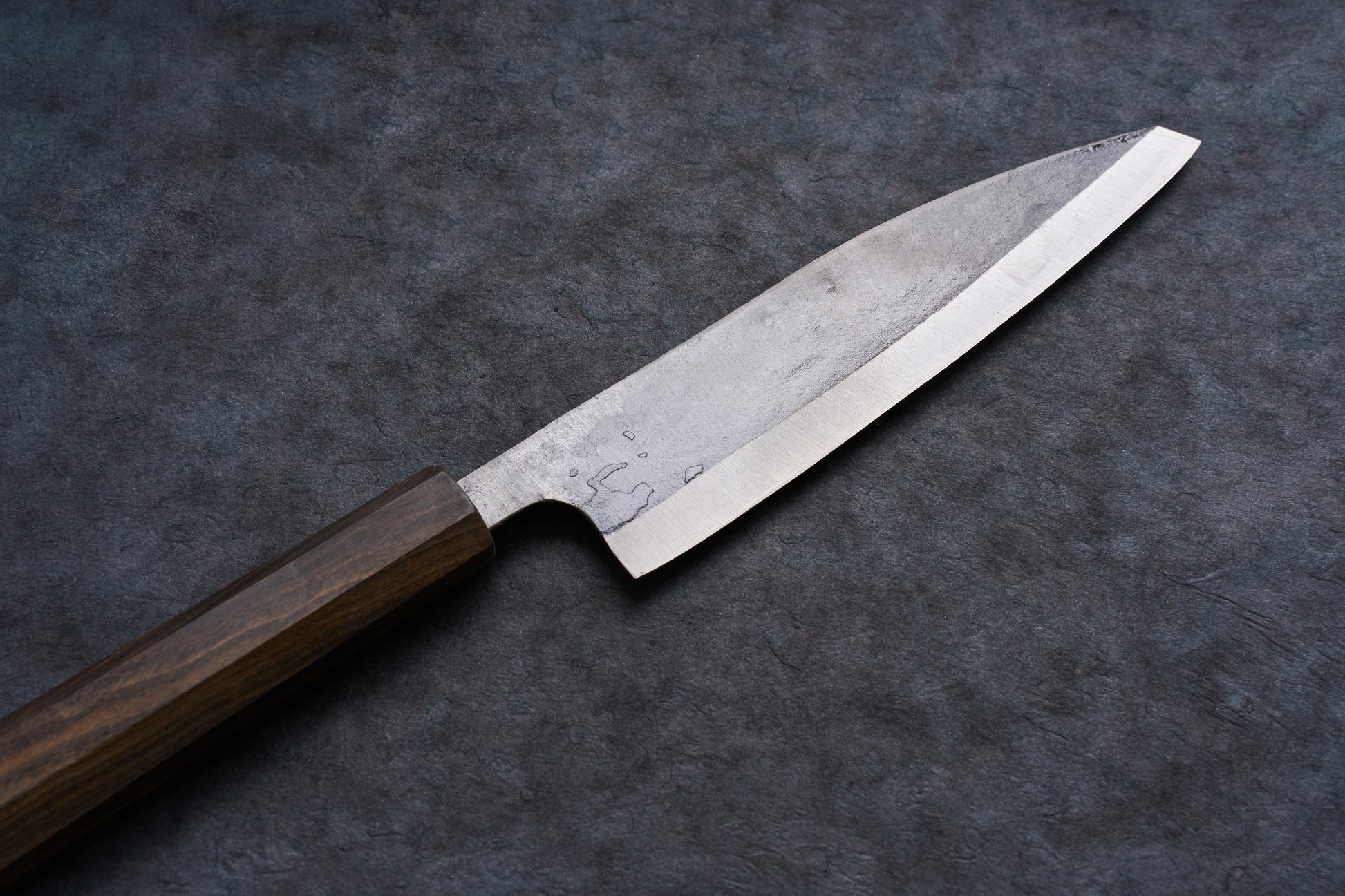 Fukamizu Ginsan Satuma no Kami Ko-Bunka 150mm knife, featuring a steel blade and dark wooden handle, displayed diagonally on a slate-like surface.