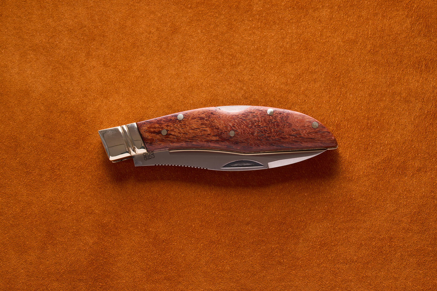 Grohmann Mini Russell Lockblade with Rosewood Handle, 4, partially open on suede, showcasing its polished bolster and serrated stainless steel blade.