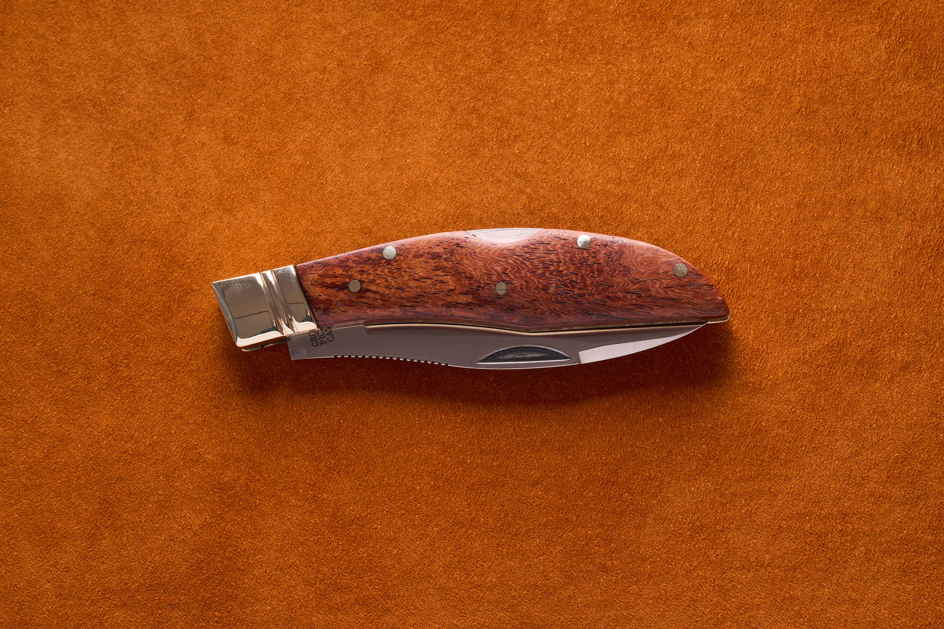 Grohmann Mini Russell Lockblade with Rosewood Handle, 4, partially open on suede, showcasing its polished bolster and serrated stainless steel blade.
