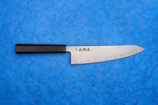 Hatsukokoro SLD Hikari Kurozome Damascus Gyuto 210mm knife with a Damascus-pattern blade and dark wooden handle on a blue background.