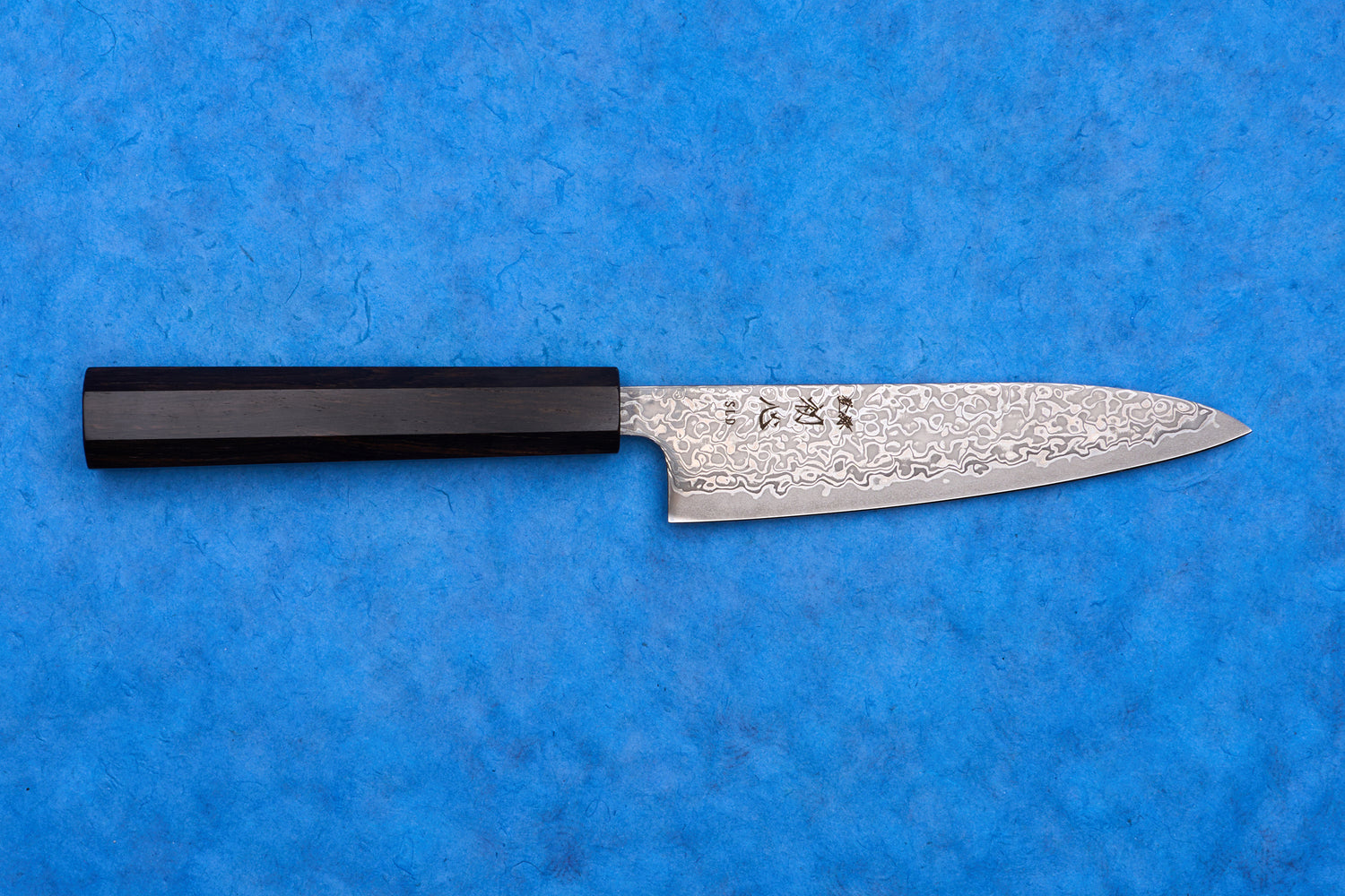 Hatsukokoro SLD Hikari Kurozome Damascus Petty 130mm knife with dark wooden handle, showcasing Damascus steel's wavy pattern, ideal for precise chopping tasks.