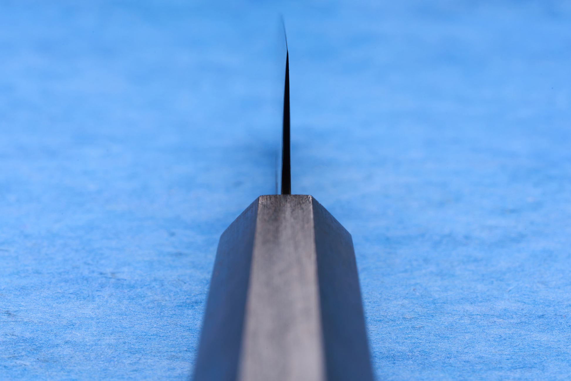 Hatsukokoro SLD Hikari Kurozome Damascus Petty 130mm knife, macro view of sharpened blade edge on blue mat, ideal for precise cutting tasks.