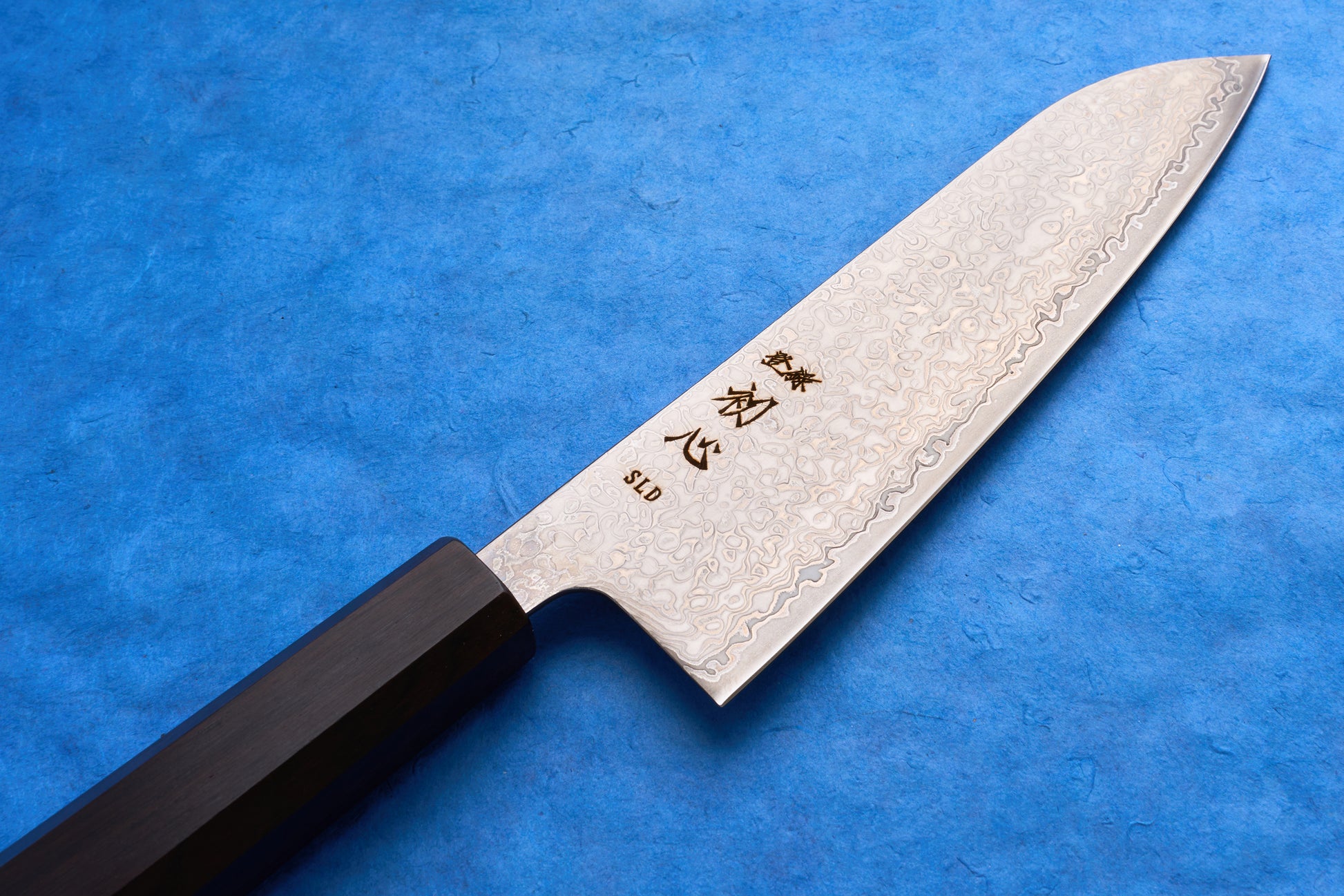 Hatsukokoro SLD Hikari Kurozome Damascus Santoku 170mm knife with patterned steel blade and octagonal dark wood handle, ideal for slicing, dicing, and mincing.