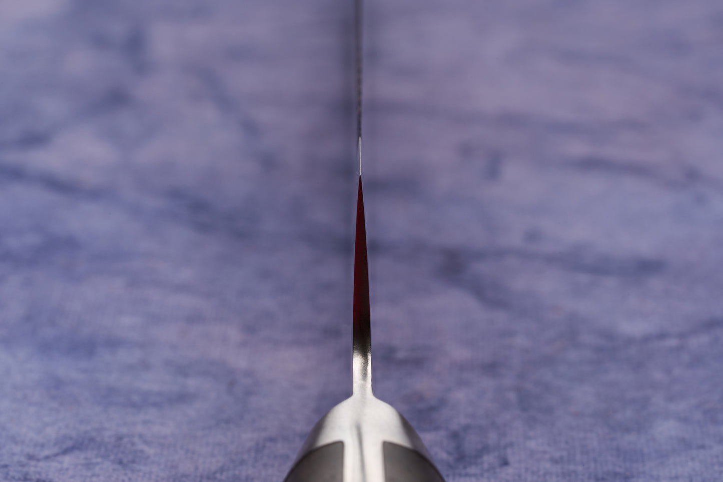 Hazaki Classic Black Bread Knife 240mm, expertly forged in Seki, Japan, features a razor-sharp, serrated blade edge-on view, with a sleek handle partially visible, set against a cloth background.