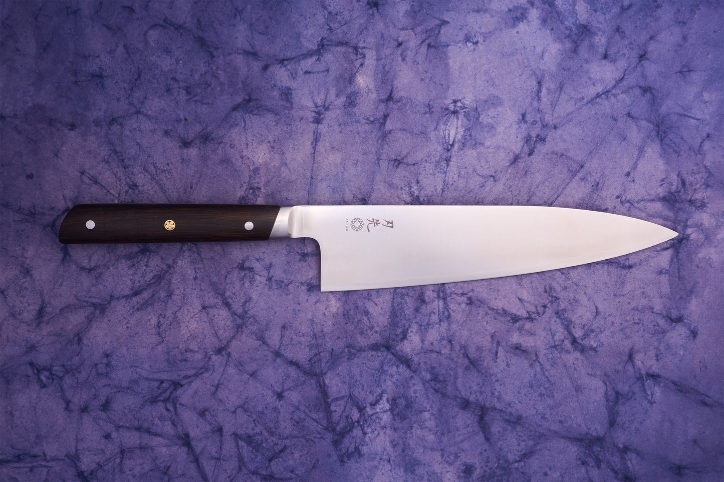 Hazaki Classic Black Gyuto 210mm knife with a stainless steel blade featuring Japanese markings and a dark wooden handle, lying on a purple textured surface, embodies expert Japanese craftsmanship and Canadian woodwork.