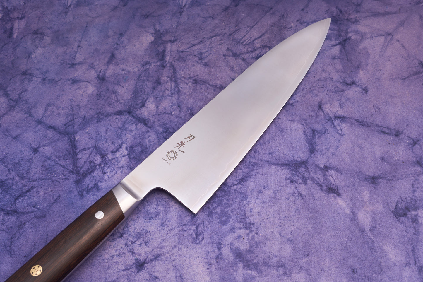 Hazaki Classic Black Gyuto 210mm features a polished stainless steel blade with Japanese characters and a dark wooden handle, lying on a purple fabric background, embodying Japanese craftsmanship and Canadian woodwork.