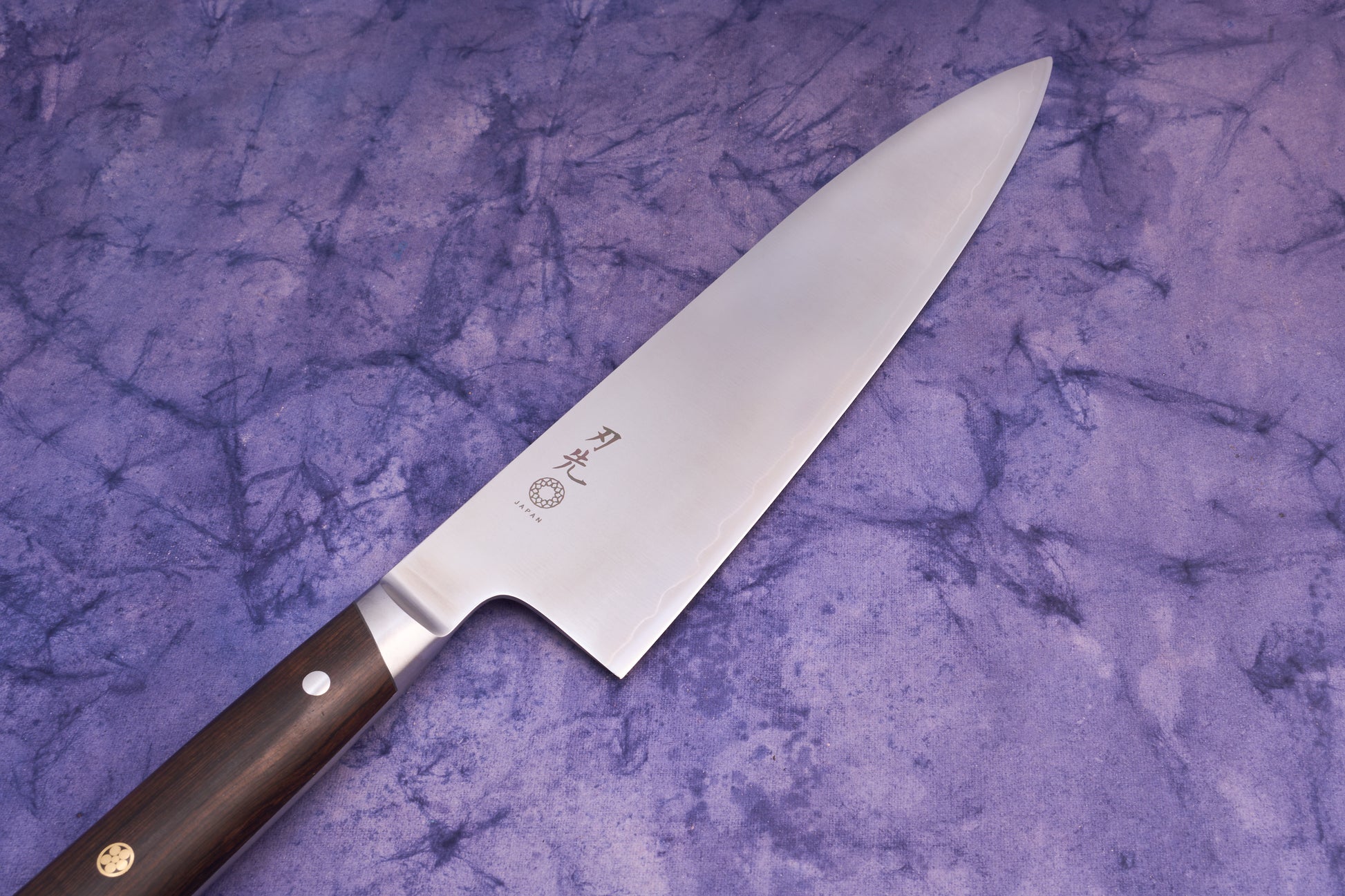 Hazaki Classic Black Gyuto 210mm features a polished stainless steel blade with Japanese characters and a dark wooden handle, lying on a purple fabric background, embodying Japanese craftsmanship and Canadian woodwork.