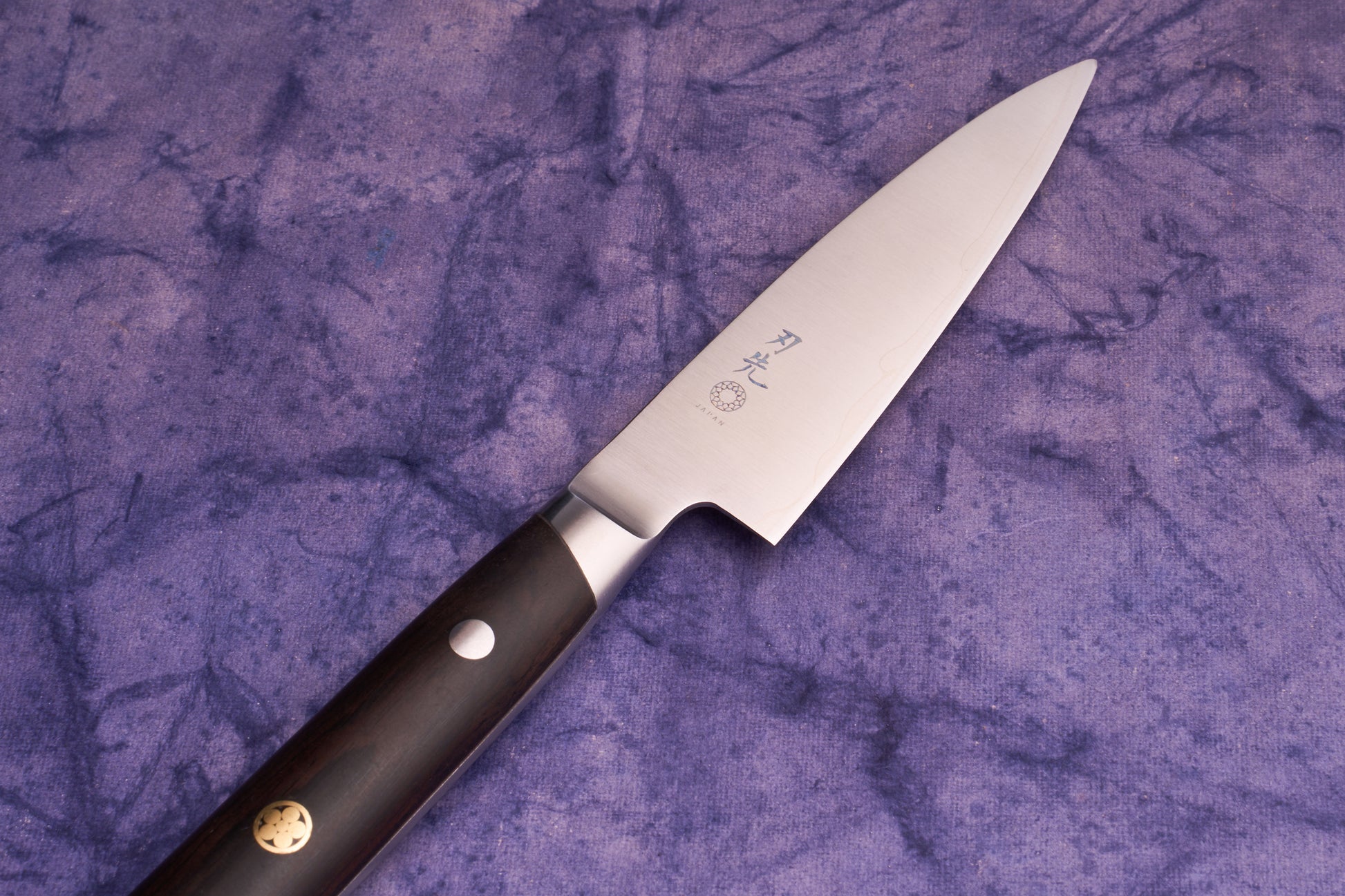 Hazaki Classic Black Petty 90mm knife with a stainless steel blade featuring Japanese characters and a dark wood handle, resting on a purple cloth background, showcasing its high-end craftsmanship.