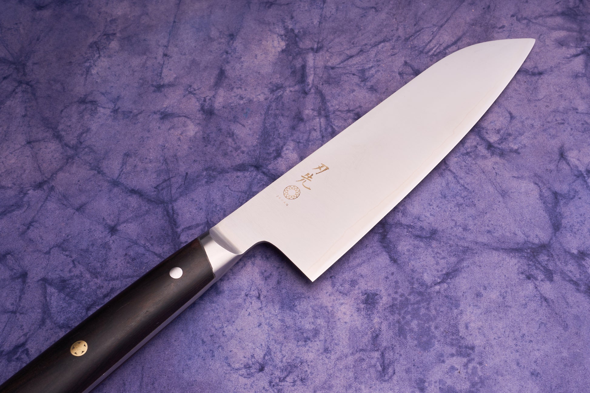 Hazaki Classic Black Santoku 180mm knife with a polished stainless-steel blade etched with Japanese characters, and a dark wooden handle with metal rivets, resting on a mottled cloth background.