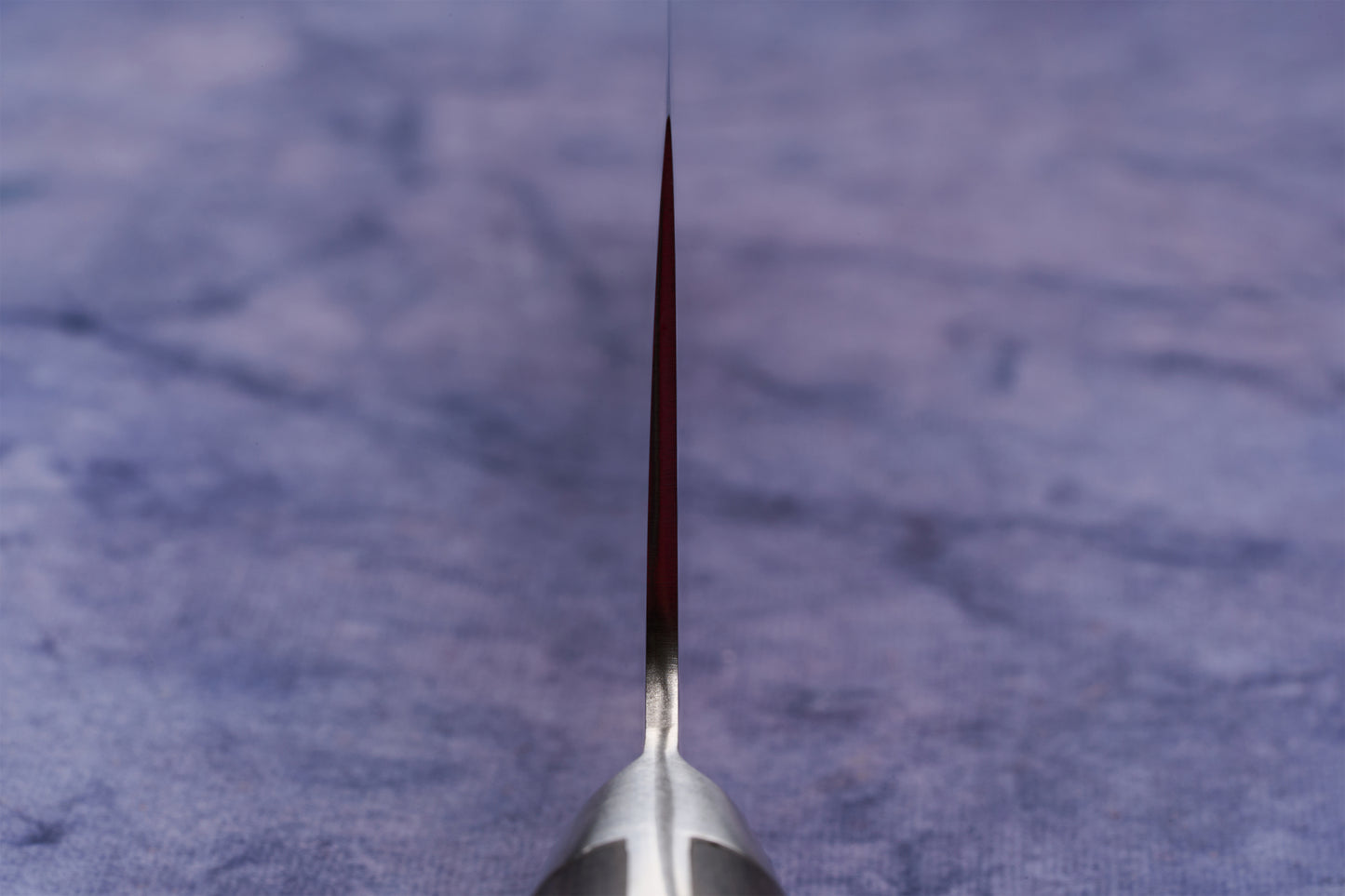 Hazaki Classic Black Santoku 180mm knife, viewed from the handle down the spine, showcasing its thin blade edge resting on a blue cloth. The blade is forged from high-end Japanese steel.