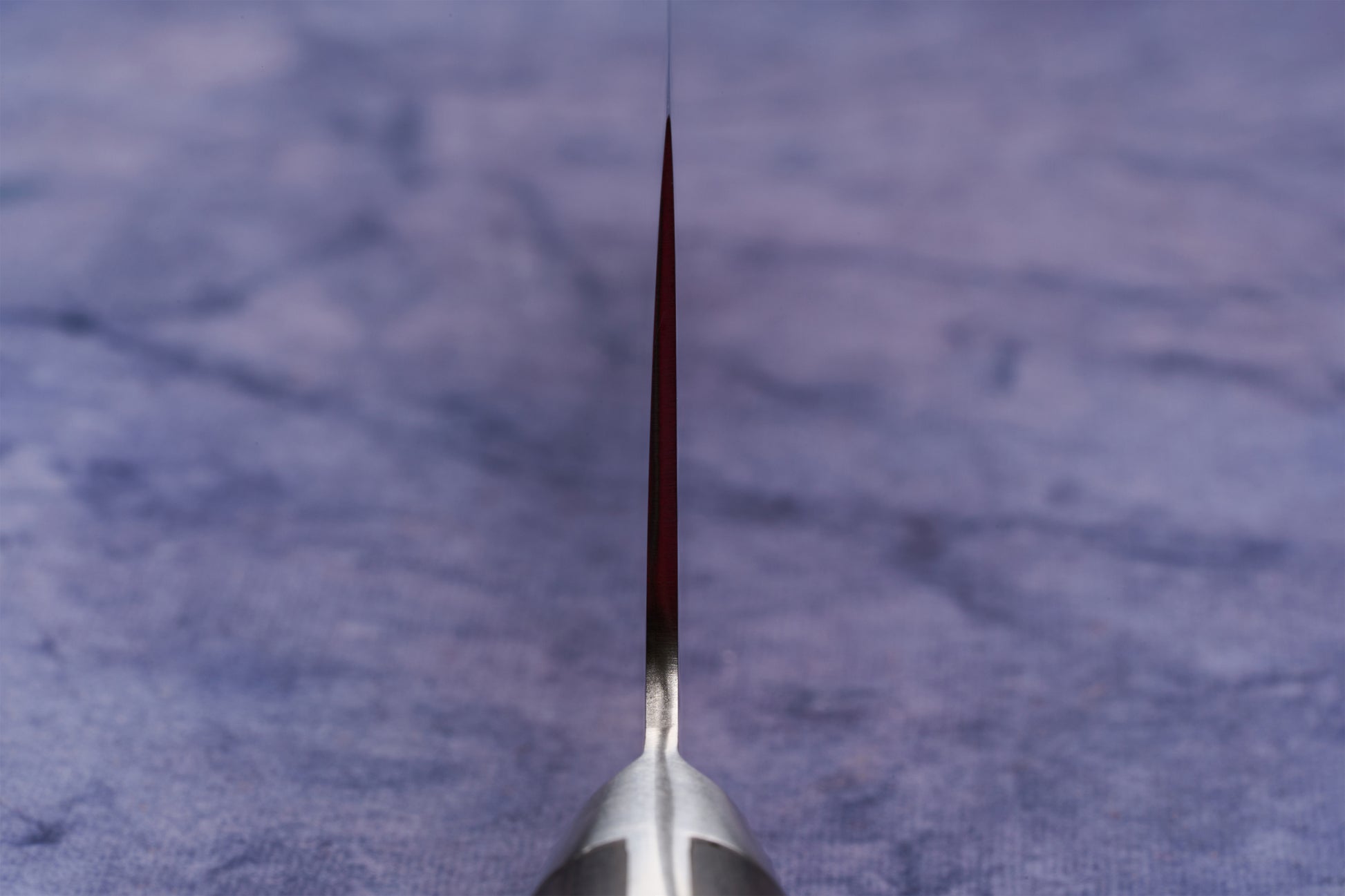 Hazaki Classic Black Santoku 180mm knife, viewed from the handle down the spine, showcasing its thin blade edge resting on a blue cloth. The blade is forged from high-end Japanese steel.