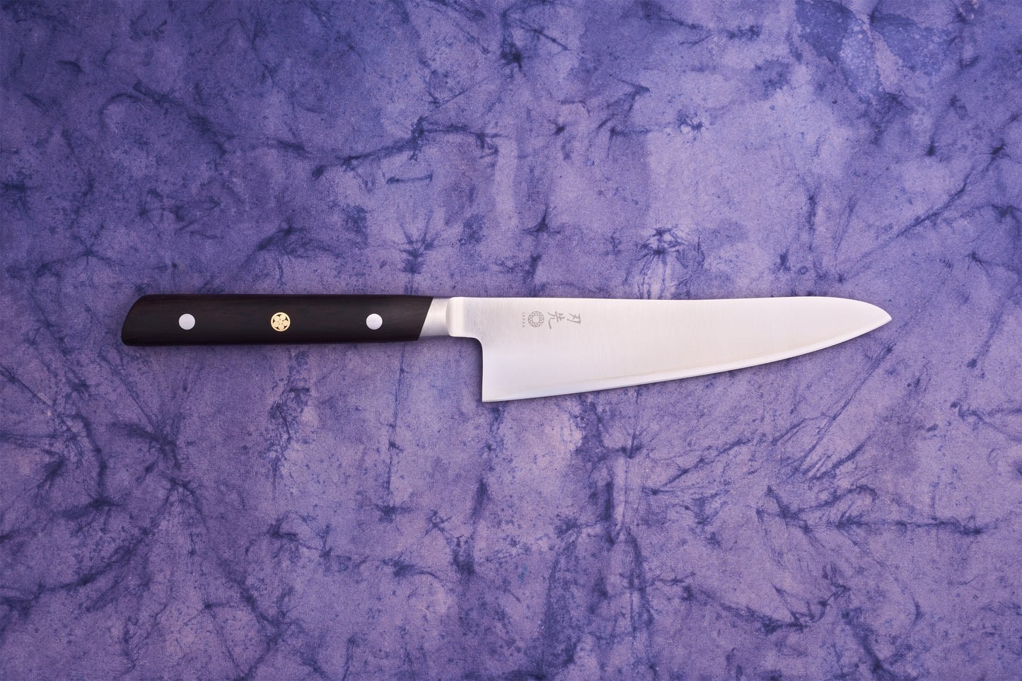 Hazaki Classic Black Utility 135mm knife with a long, straight-edged blade featuring Japanese characters, and a dark wooden handle with rivets and a brass pin, on a purple cloth background.