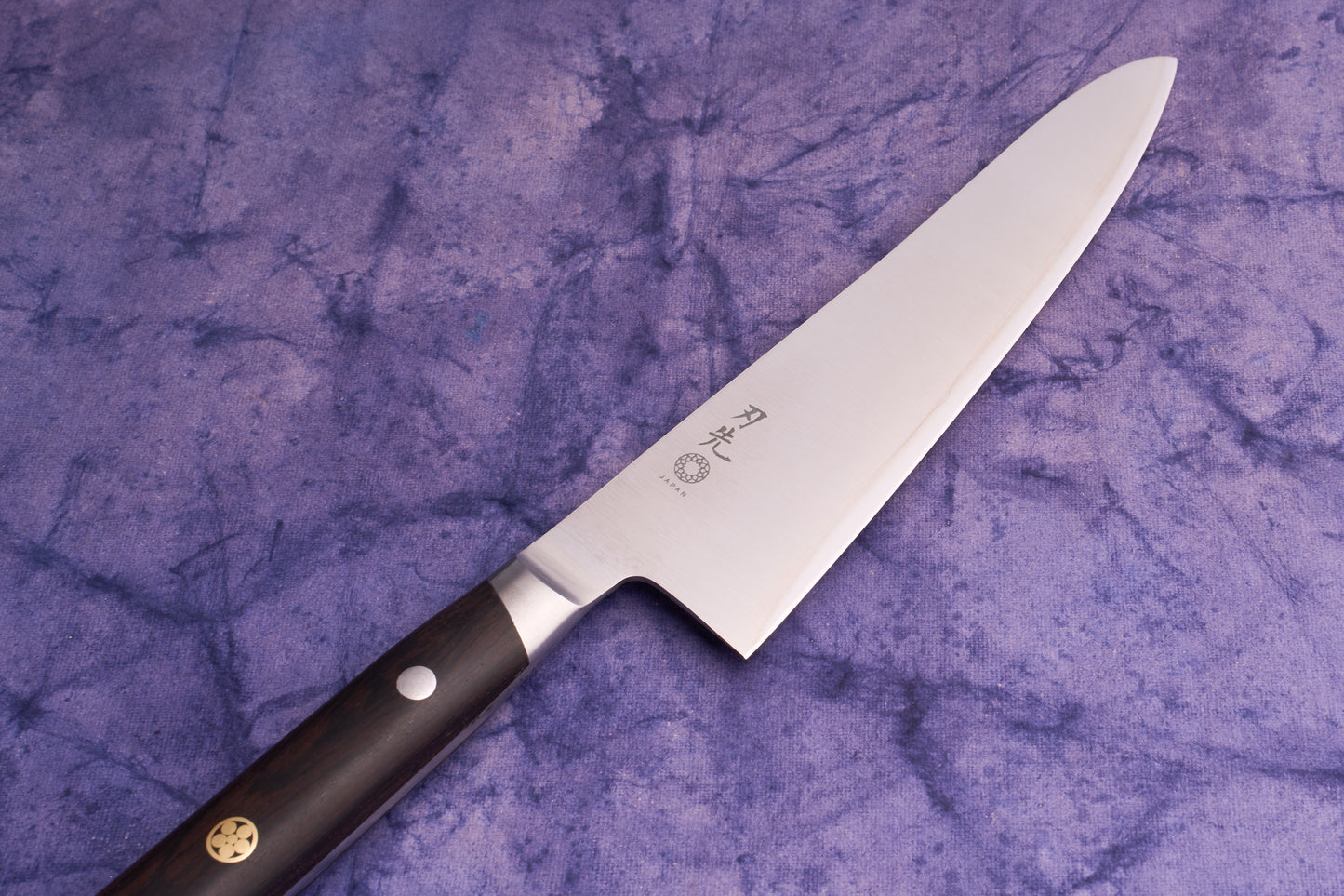 Hazaki Classic Black Utility 135mm knife with a stainless steel blade featuring Japanese characters and a Japan stamp, complemented by a dark wood handle with metal rivets, laid on a purple cloth.