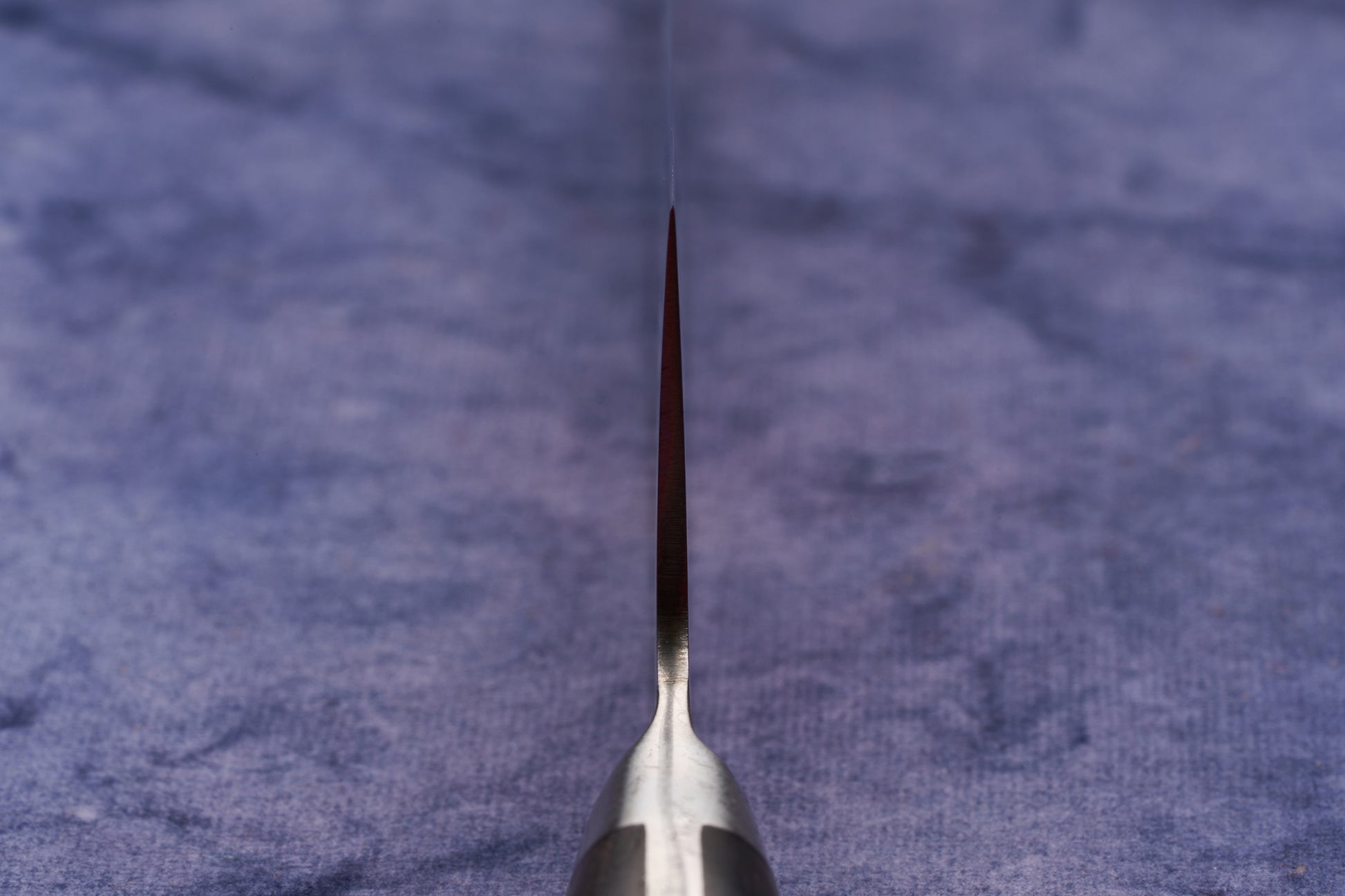 Hazaki Classic Black Utility 135mm knife, standing edge-up on a blue cloth, showcases its thin, sharp blade expertly forged in Japan. The handle, crafted from Canadian wood, complements its sleek design.