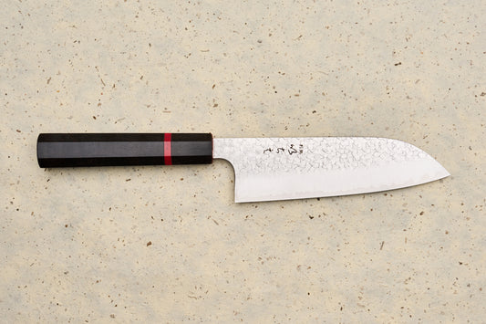 ICHIE x Shibata Knives SG2 Tsuchime Santoku 165mm, featuring a hammered finish and octagonal wooden handle, displayed on a light speckled surface.