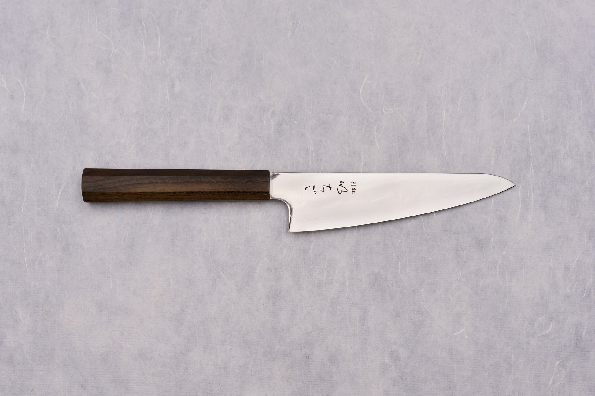 ICHIGO SLD Migaki Gyuto 150mm knife with a polished high-carbon blade and dark wooden octagonal handle, featuring Japanese kanji characters, displayed on a textured surface, exemplifying Japanese craftsmanship.