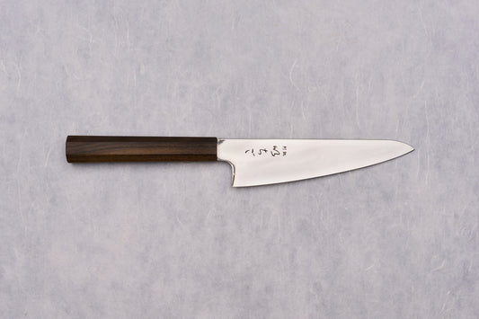 ICHIGO SLD Migaki Gyuto 150mm knife with a polished high-carbon blade and dark wooden octagonal handle, featuring Japanese kanji characters, displayed on a textured surface, exemplifying Japanese craftsmanship.