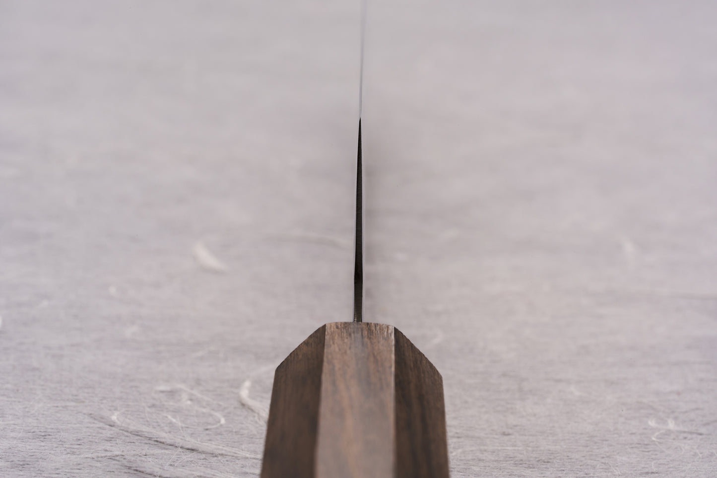 ICHIGO SLD Migaki Petty 130mm knife with a polished, mirror-like blade and dark wooden handle, showcased edge-on against a light surface, exemplifying refined craftsmanship and cutting precision.