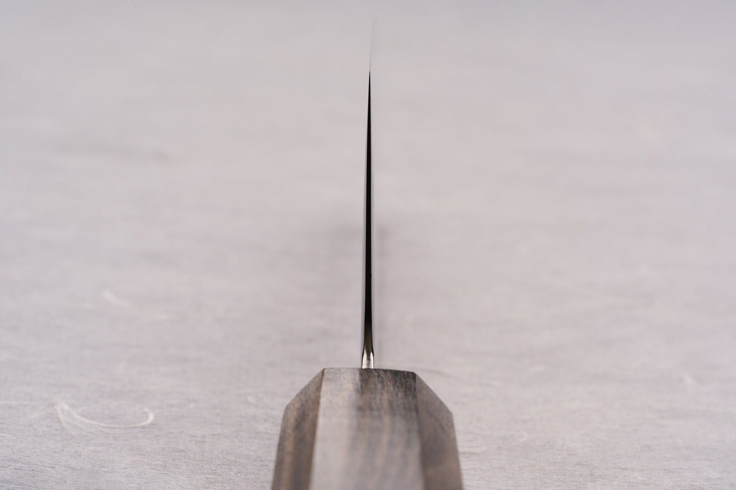 ICHIGO SLD Migaki Santoku 170mm knife features a polished blade and dark wooden handle, resting vertically. This versatile, thin-edged knife excels in slicing, dicing, and mincing, enhancing your cooking experience.