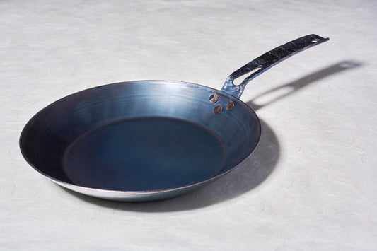 Leechtown Blacksmith Co. Medium Flamerider Carbon Steel pan, featuring a bluish-seasoned finish with a riveted, hammered-style handle, ideal for versatile cooking.