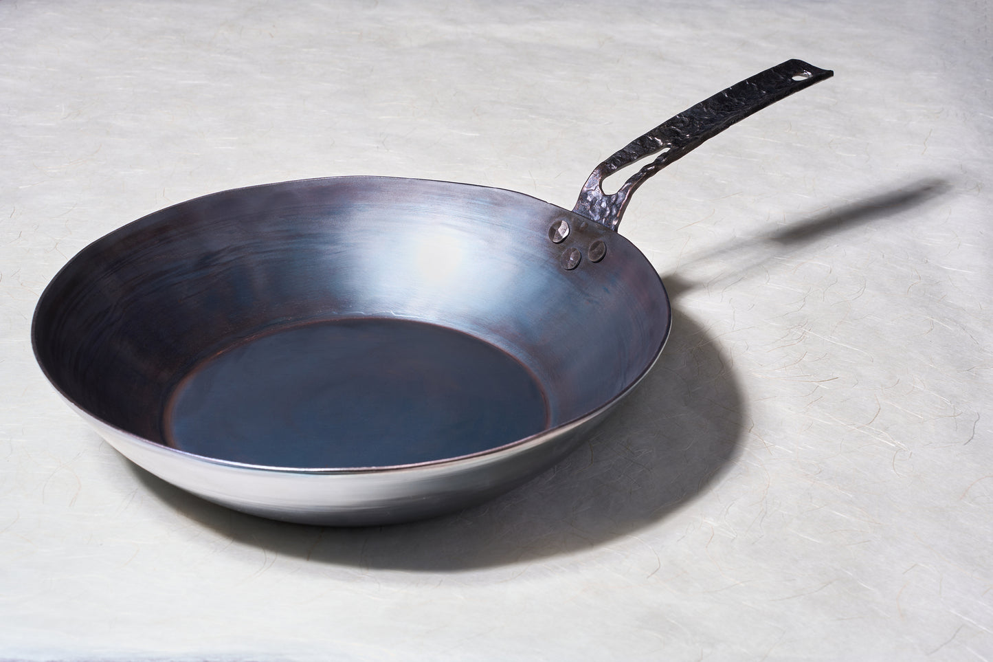 Leechtown Blacksmith Co. Mokwok Carbon Steel Pan Small with hammered-steel handle, rivets, and hanging loop, ideal for versatile cooking methods.