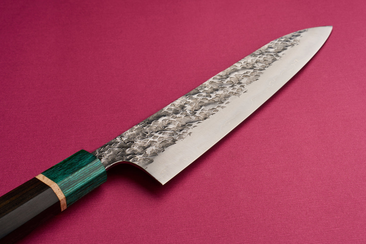 Makoto Kurosaki SPG STRIX Samidorizuki Gyuto 210mm displayed against a plain surface, featuring a long, hammered blade and an octagonal deep green wooden handle, embodying the craftsmanship of Japanese kitchen knives.