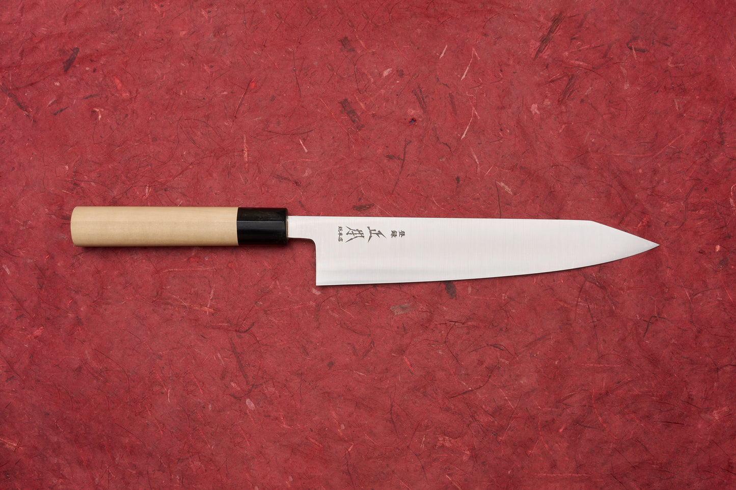 Masamoto KS Hongasumi Kiritsuke Gyuto 210mm knife with a polished, slender blade etched with Japanese characters and a wooden handle, displayed on a textured red background, embodying precision and craftsmanship.