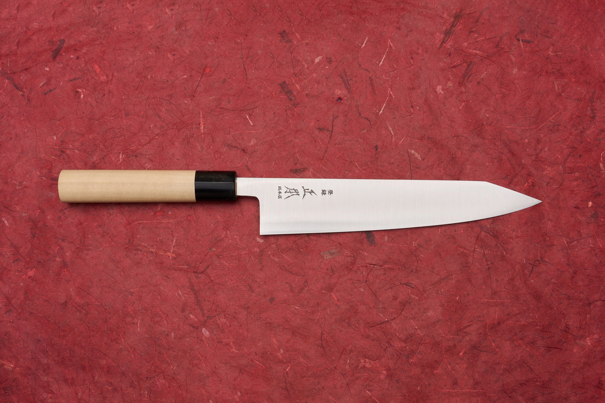 Masamoto KS Hongasumi Kiritsuke Gyuto 210mm knife with a polished, slender blade etched with Japanese characters and a wooden handle, displayed on a textured red background, embodying precision and craftsmanship.