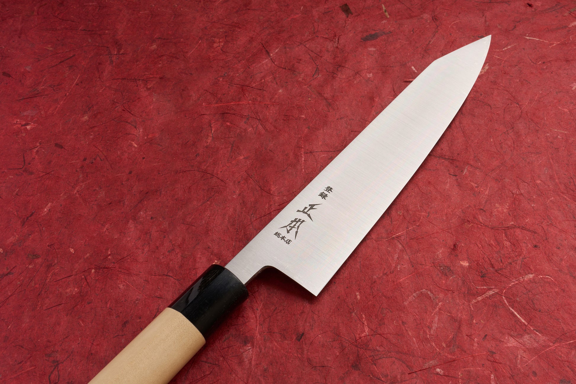 Masamoto KS Hongasumi Kiritsuke Gyuto 210mm with a slender, satin-finished blade, laser-etched kanji near the heel, and a wa-style handle, ideal for precision slicing, displayed on a red background.