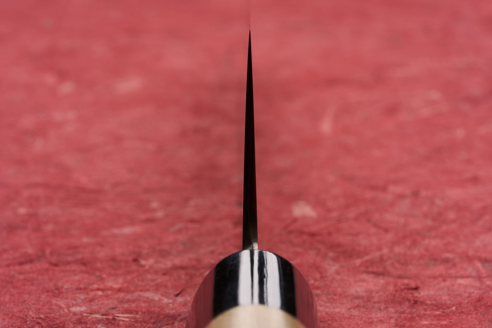 Masamoto KS Hongasumi Kiritsuke Gyuto 240mm knife, thin blade rising from dark bolster and wooden handle, showcased on a red surface, epitomizing precision and craftsmanship from legendary Tokyo-based knifemaker.